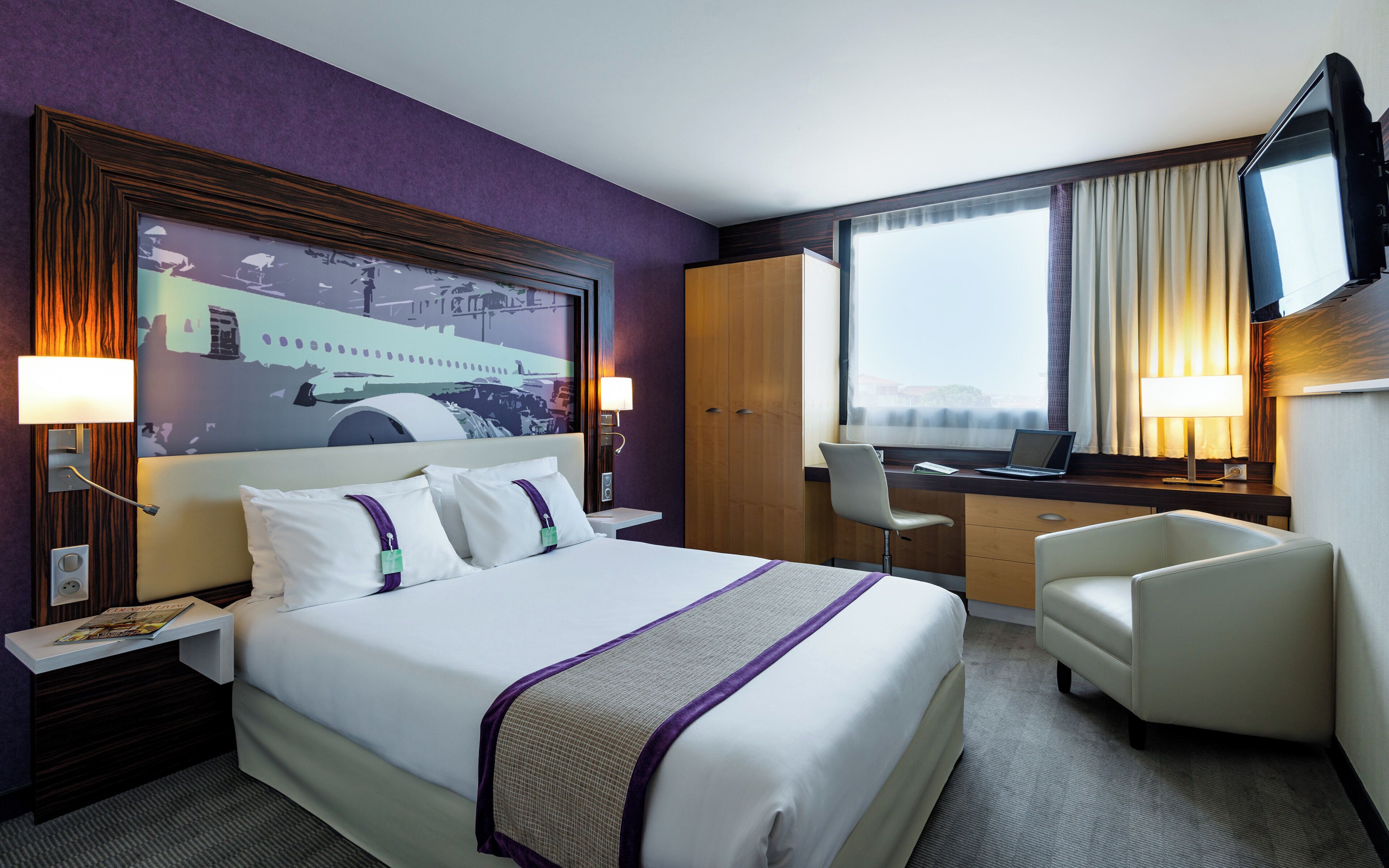 A hotel room with a large bed, a desk, a chair, and a television.