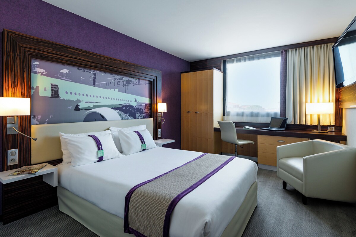 A hotel room with a large bed, a desk, a chair, and a television.