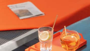 Escena junto a la piscina con dos bebidas sobre una mesa, una revista y una silla de descanso.