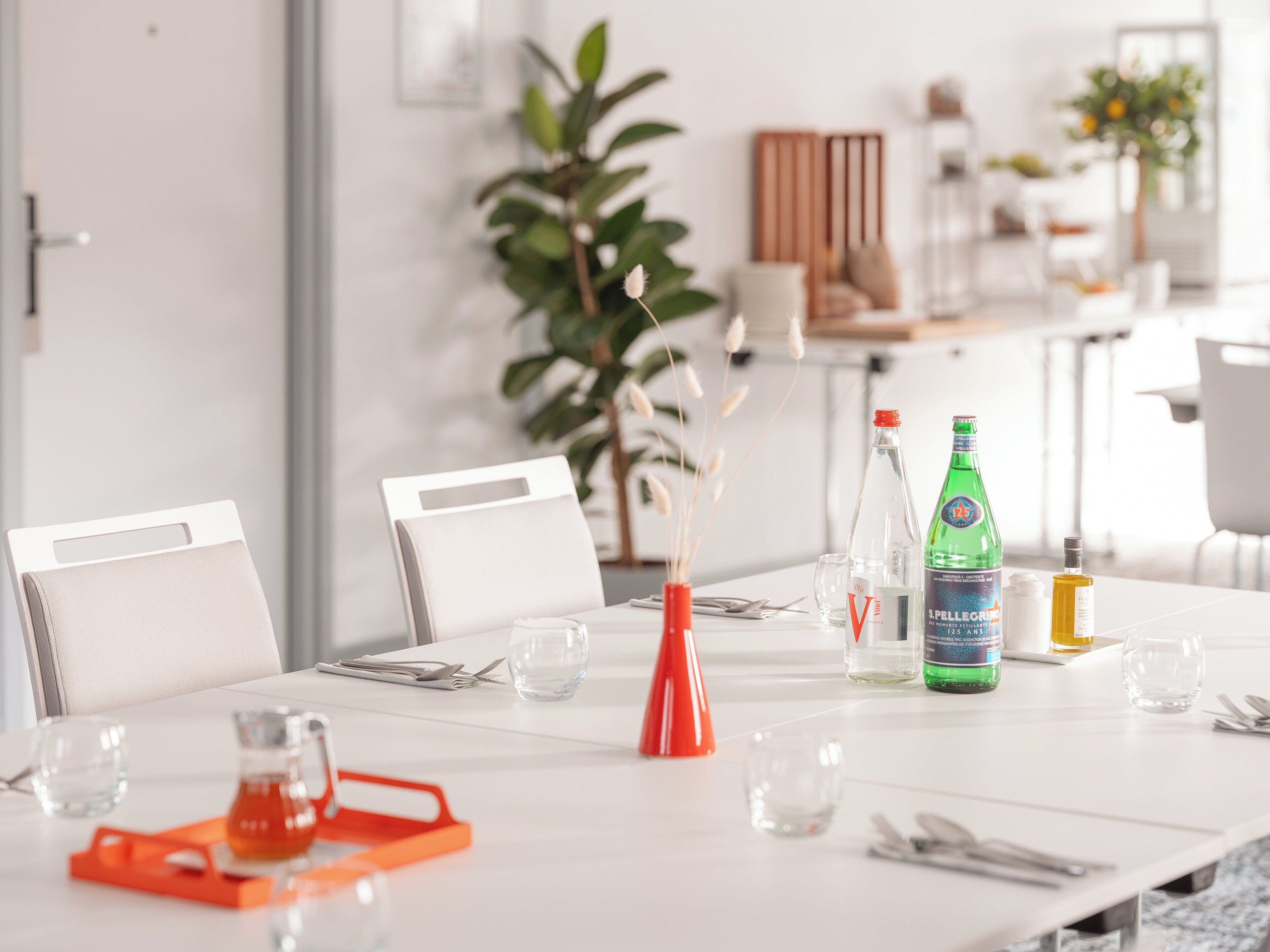 A dining table set with chairs, a vase with dried plants, and bottles of beverages.