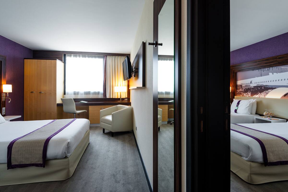 Ein Hotelzimmer mit zwei Betten, einem Schreibtisch, einem Stuhl und einem großen Spiegel.