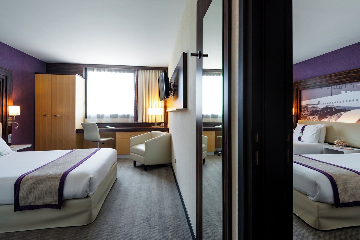 A hotel room with two beds, a desk, a chair, and a large mirror.