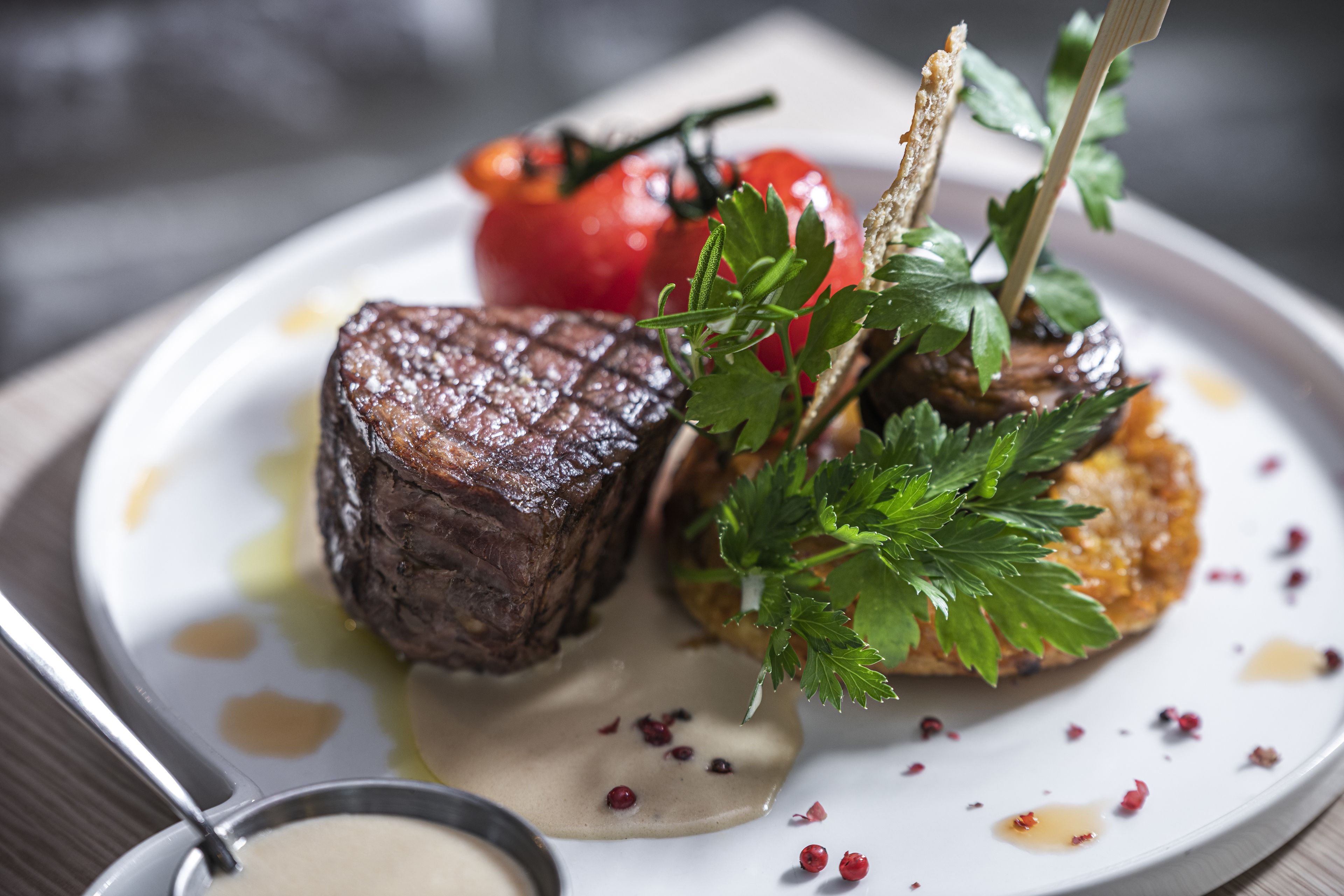 A plate with a steak, a tomato, and a garnish.