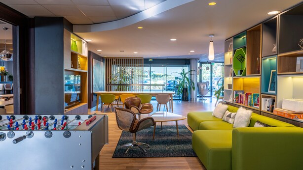 A modern lounge area with a foosball table, comfortable seating, and a well-organized bookshelf. - Holiday Inn Toulouse Airport by IHG (Blagnac)