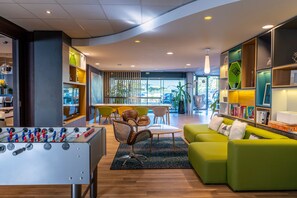A modern lounge area with a foosball table, comfortable seating, and a well-organized bookshelf. - Holiday Inn Toulouse Airport by IHG (Blagnac)