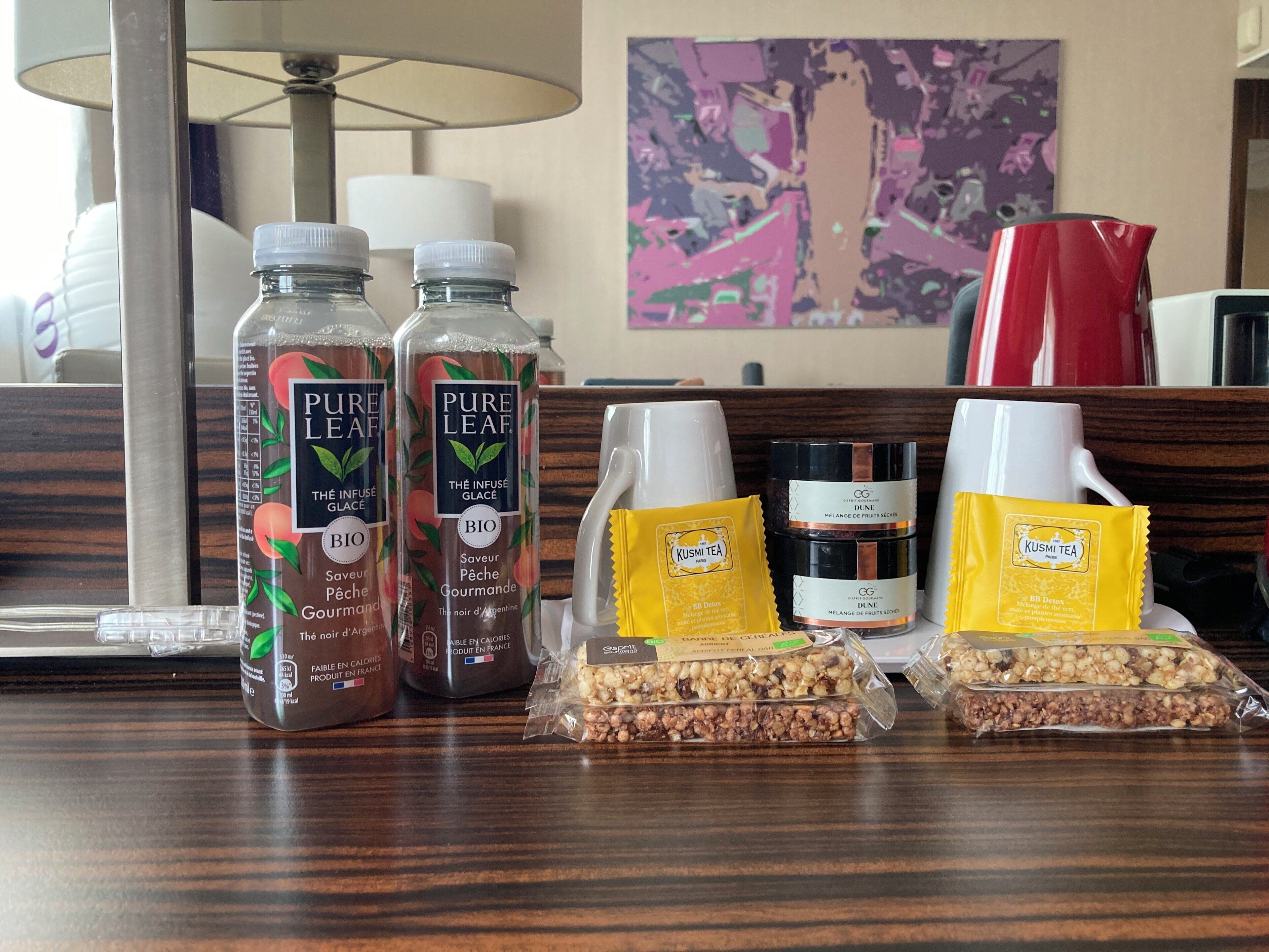A hotel reception area with a wooden counter displaying various products including bottles of Pure Leaf tea, a coffee maker, and packaged snacks.