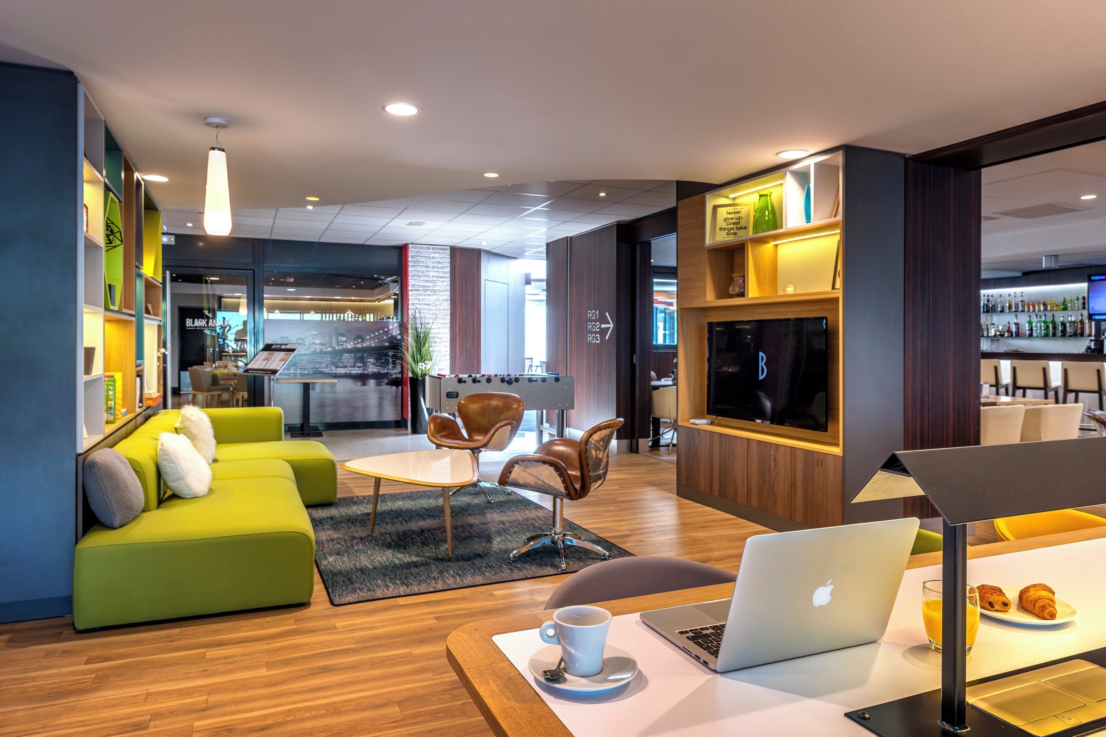 A modern lounge area with a green sofa, a coffee table, a laptop, and a breakfast tray with croissants.