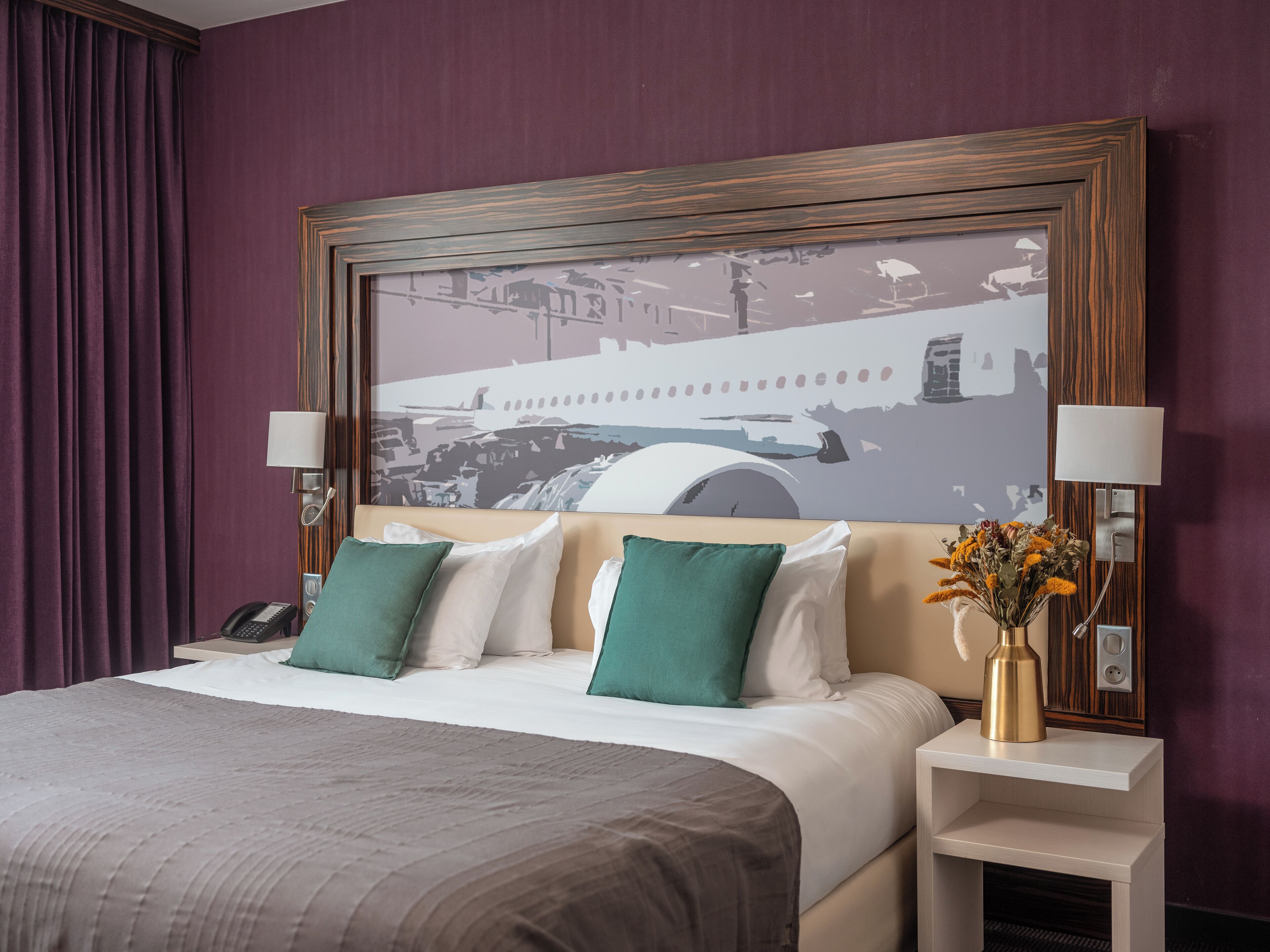 Ein Hotelzimmer mit einem großen Bett, zwei Nachttischlampen, einem Nachttisch mit Telefon und einem gerahmten Kunstwerk über dem Bett.