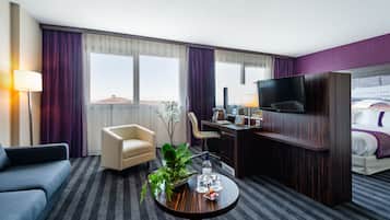 A hotel room with a sofa, a desk with a chair, a television, and a bed.