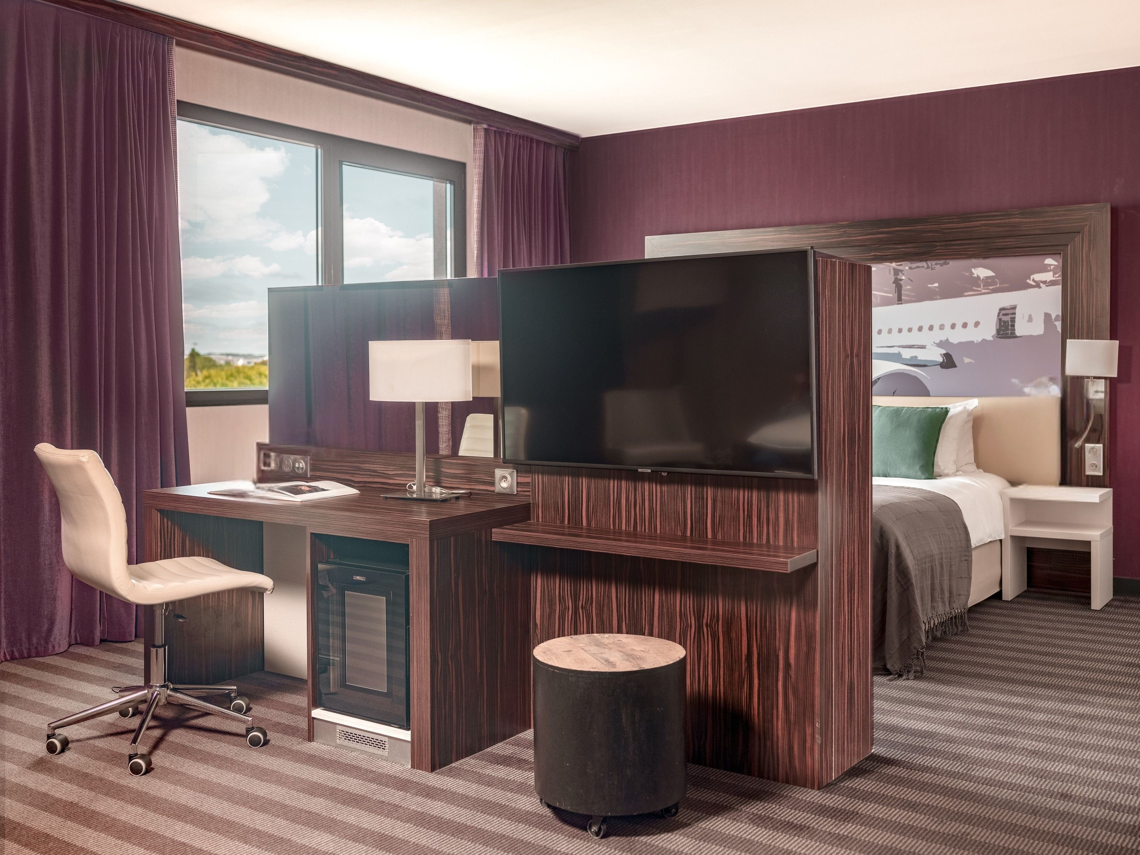 A hotel room with a desk, chair, television, and a bed.