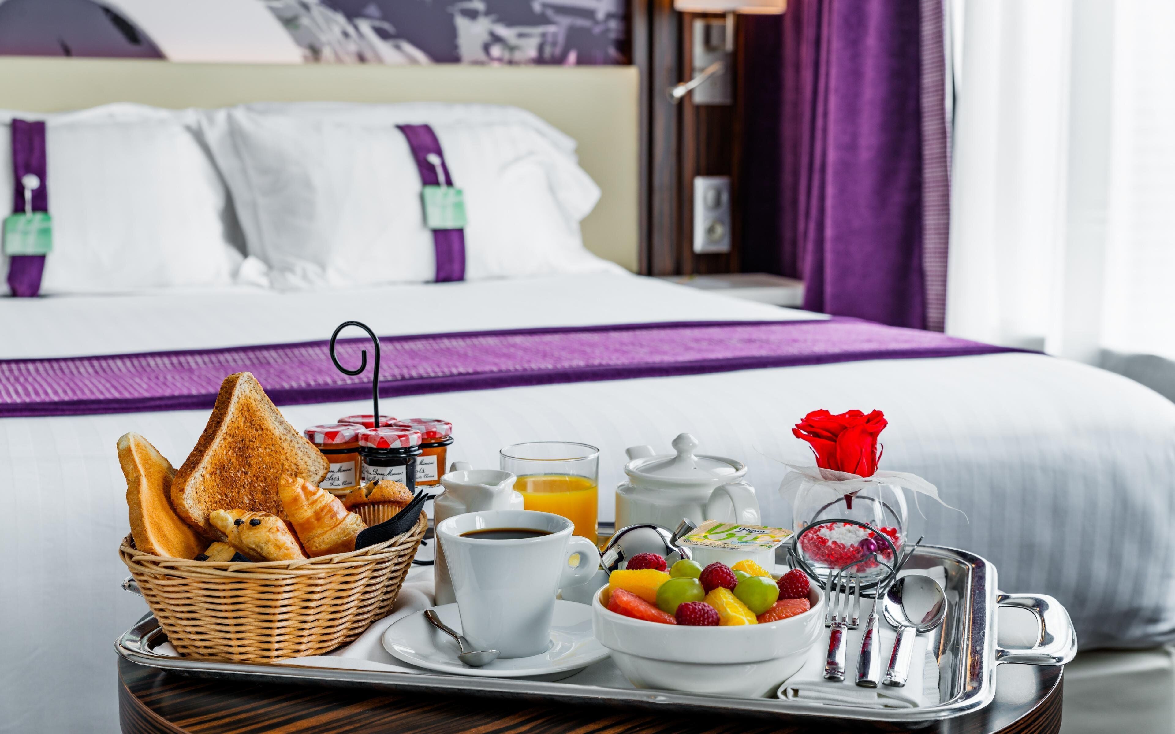 Un plateau de petit-déjeuner avec des toasts, des viennoiseries, des fruits, du café et de la confiture, posé sur une table dans une chambre d’hôtel.