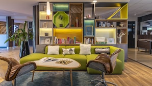 A modern living room with a green sofa, leather armchairs, a coffee table, and a bookshelf. - Holiday Inn Toulouse Airport by IHG (Blagnac)