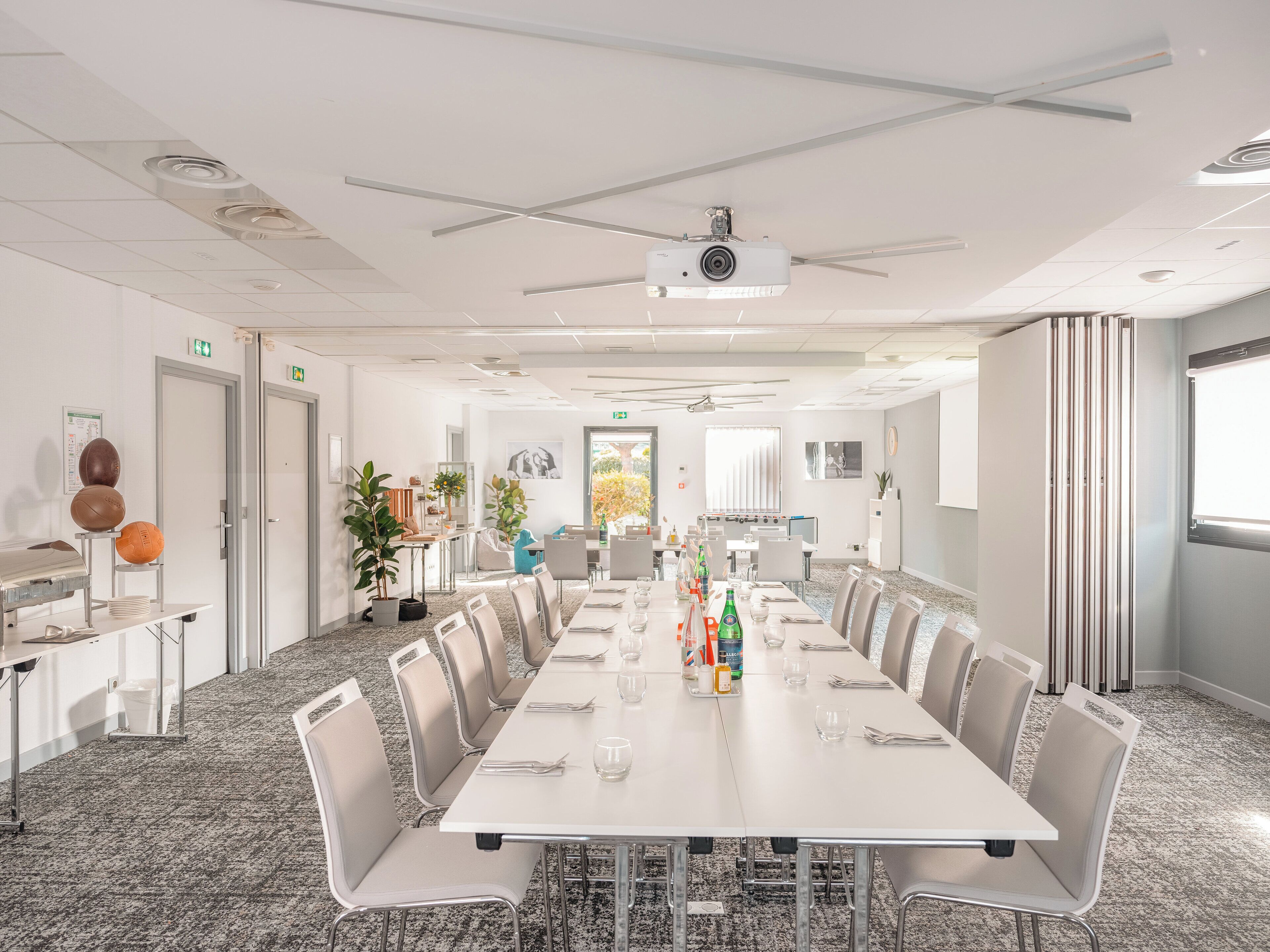A conference room with a long table, chairs, a projector, and a small plant.