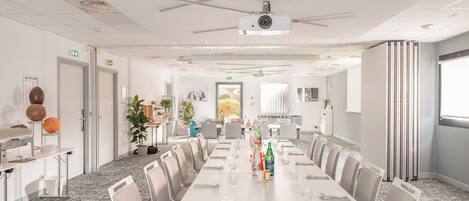 Un salón de conferencias con una larga mesa, sillas, un proyector y una planta pequeña.