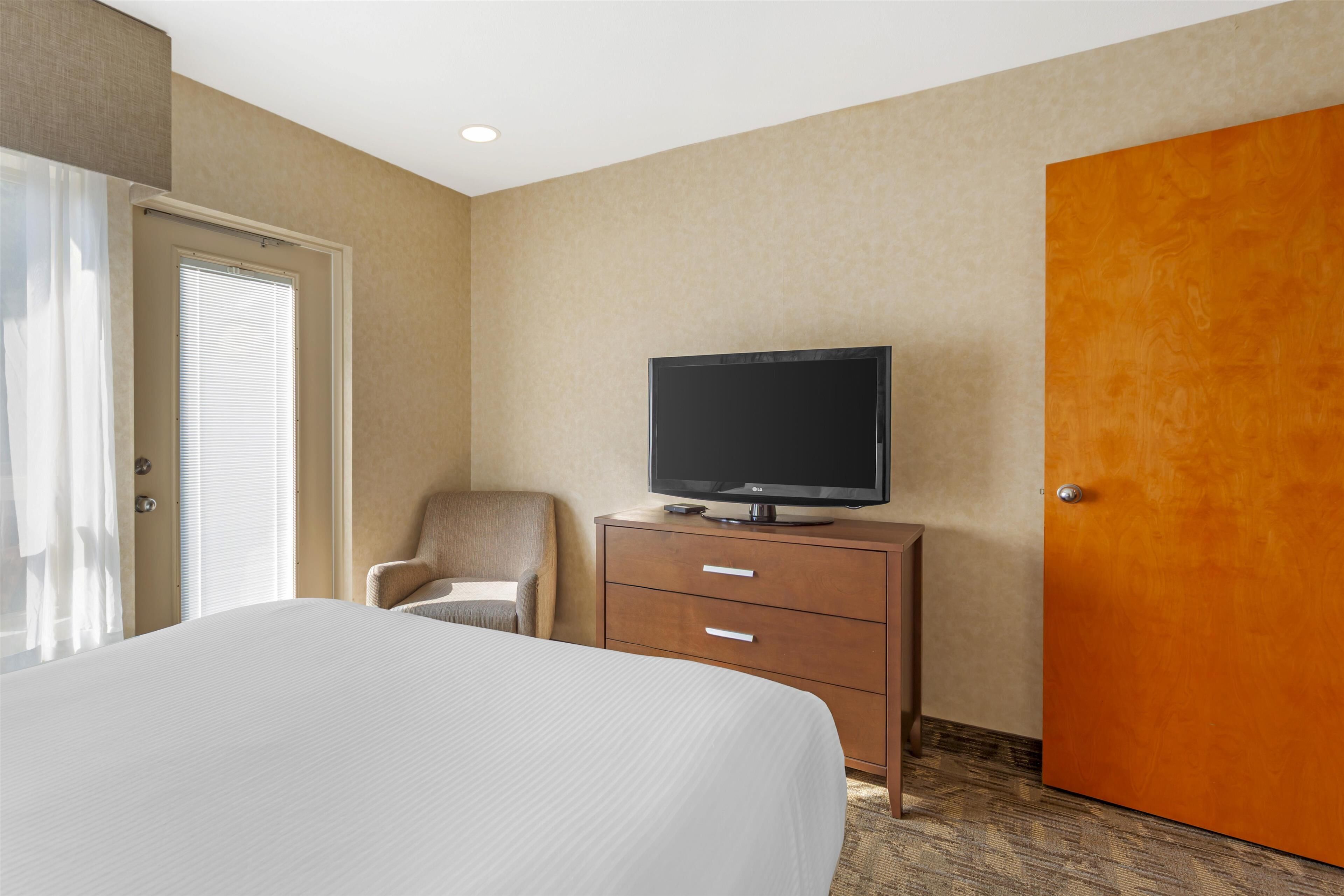 A hotel room with a bed, a television on a wooden dresser, a chair, and a door.