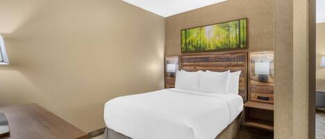 A hotel room with a large bed, a wooden headboard, a painting above the bed, a nightstand with a lamp, and a desk with a lamp.