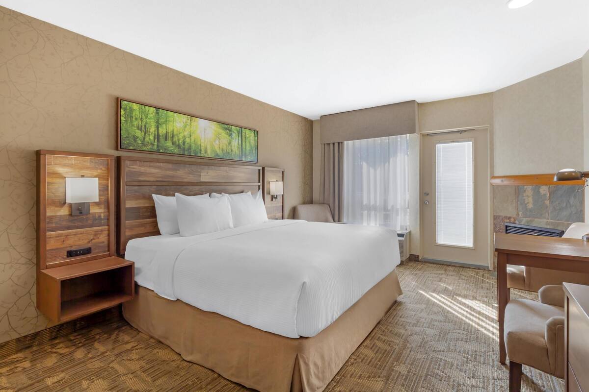 A hotel room with a large bed, a desk, a chair, a painting on the wall, and a window with curtains.