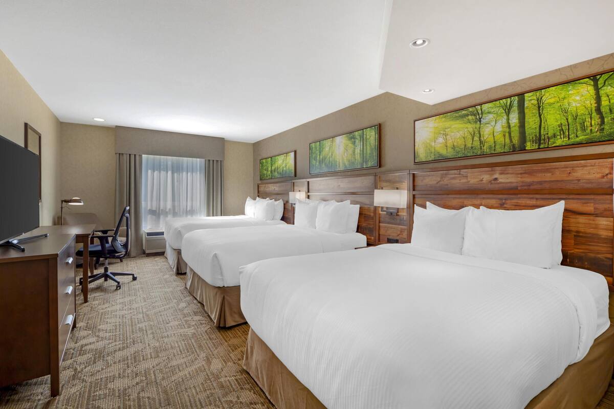 A hotel room with three beds, a desk, and a TV.