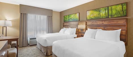 A hotel room with two beds, a desk, and a chair. There are two paintings on the wall and a window with curtains.