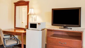 A hotel room with a wooden desk, a white refrigerator, a microwave, a television, a lamp, and a chair. - Knights Inn Mount Laurel (Mount Laurel)