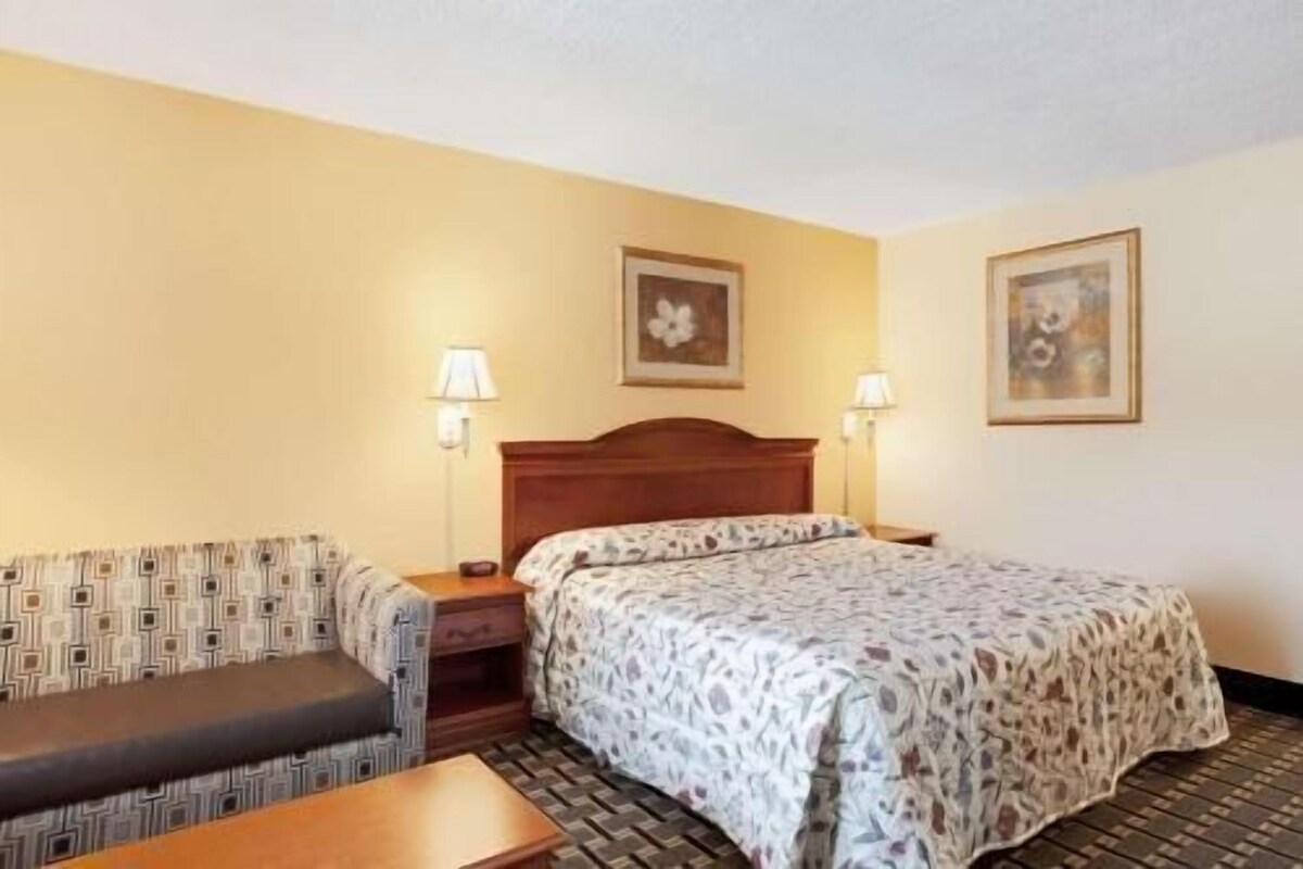 A hotel room with a bed, a sofa, a nightstand, and two wall-mounted lamps.