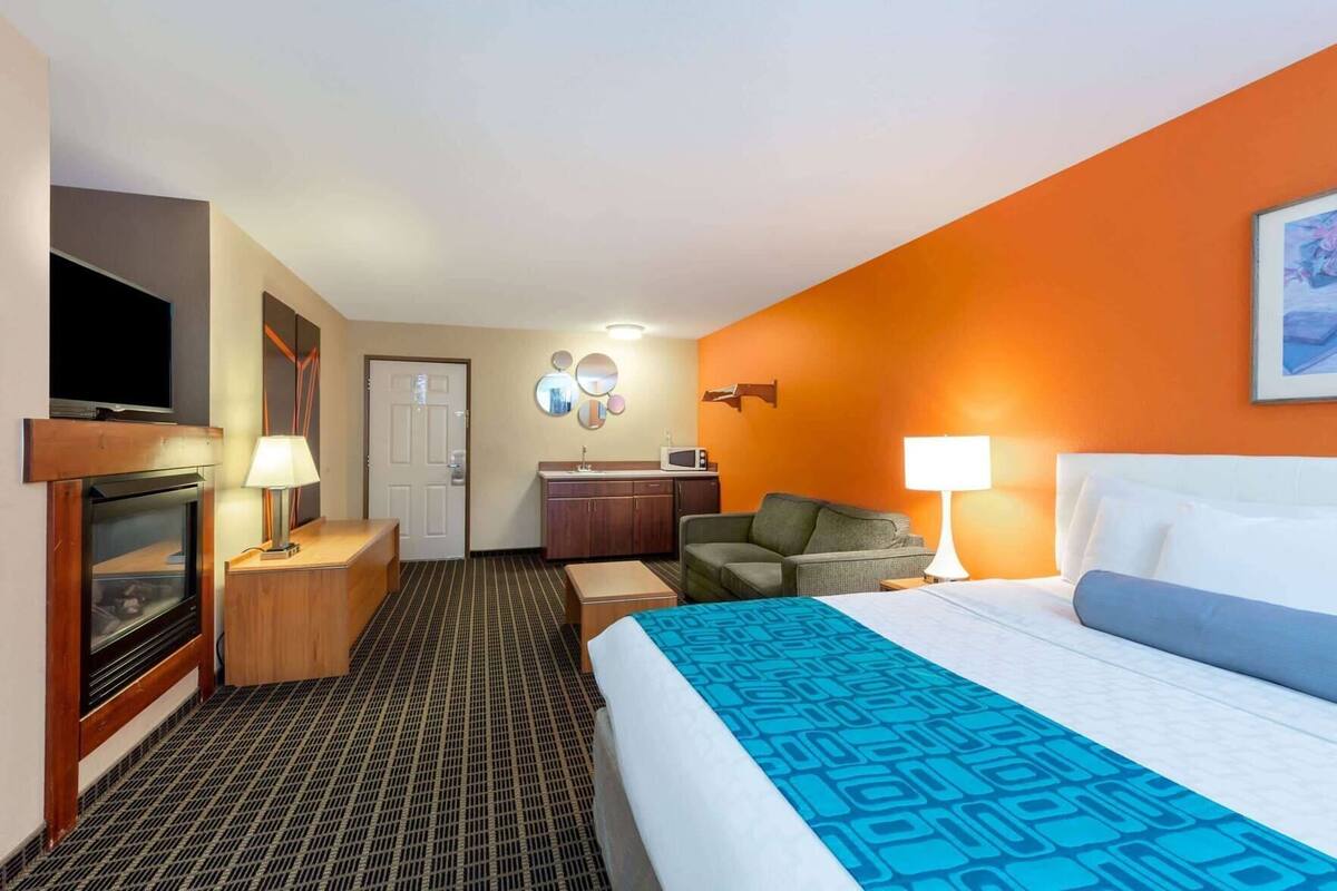 Habitación de hotel con cama, televisor, escritorio, silla, microondas y puerta.