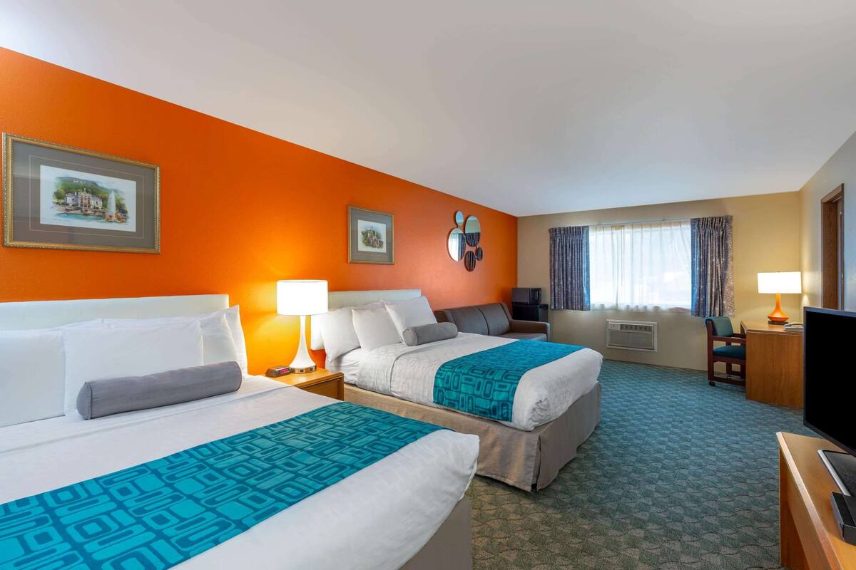Una habitación de hotel con dos camas, un escritorio, un televisor y una ventana con cortinas.