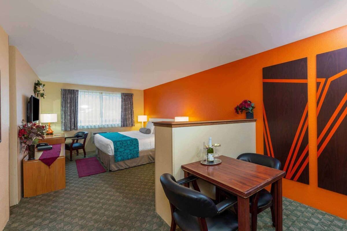 Habitación de hotel con cama, escritorio, silla, mesa y una pared naranja grande.