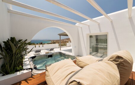 A rooftop terrace with a hot tub, beige cushions, and a view of the sea.
