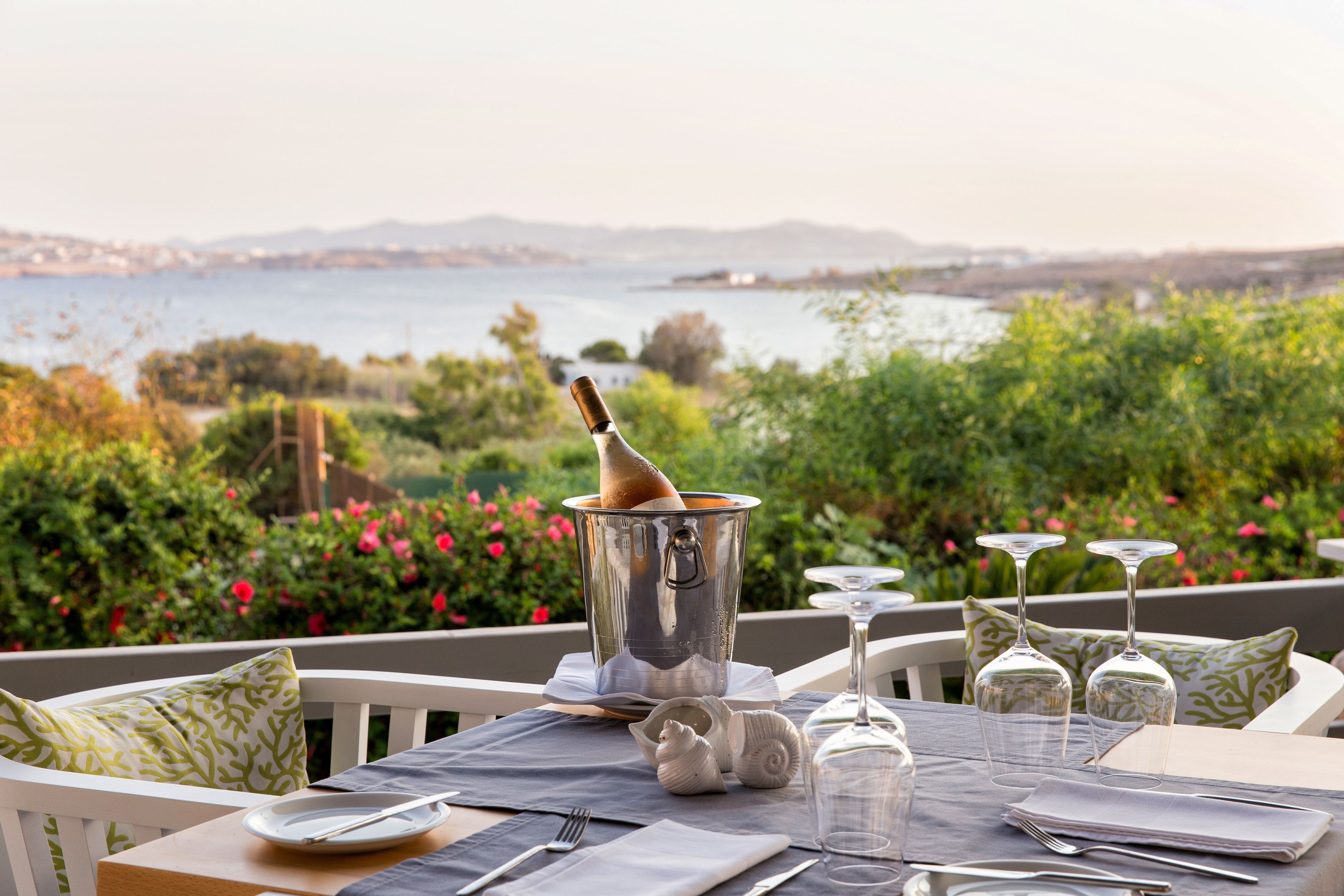 Una mesa lista para cenar con vistas al mar, una botella de champán y un paisaje panorámico.