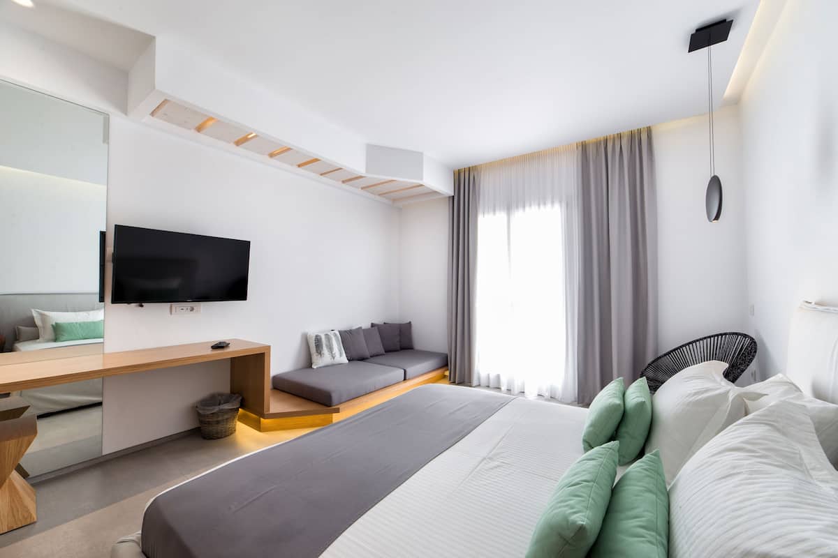 A modern hotel room with a bed, a desk, a sofa, and a TV.