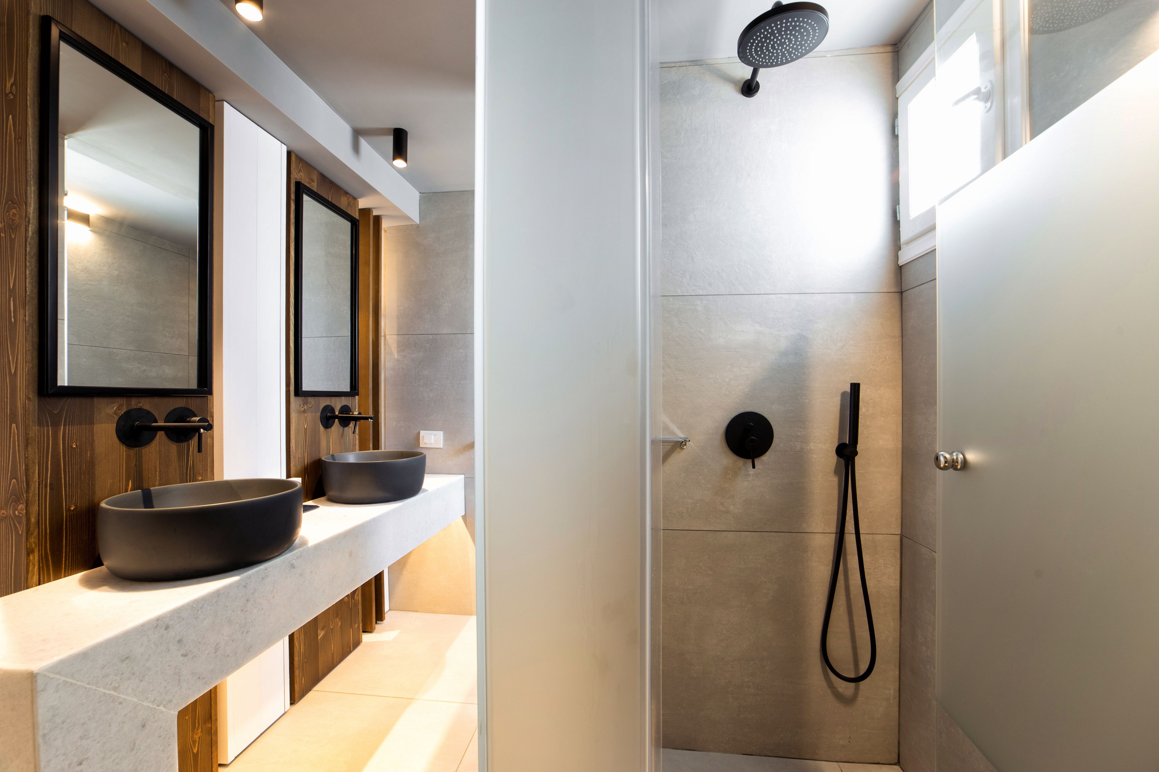 Un bagno moderno con uno specchio grande, due lavabi, una doccia con soffione manuale e un water.