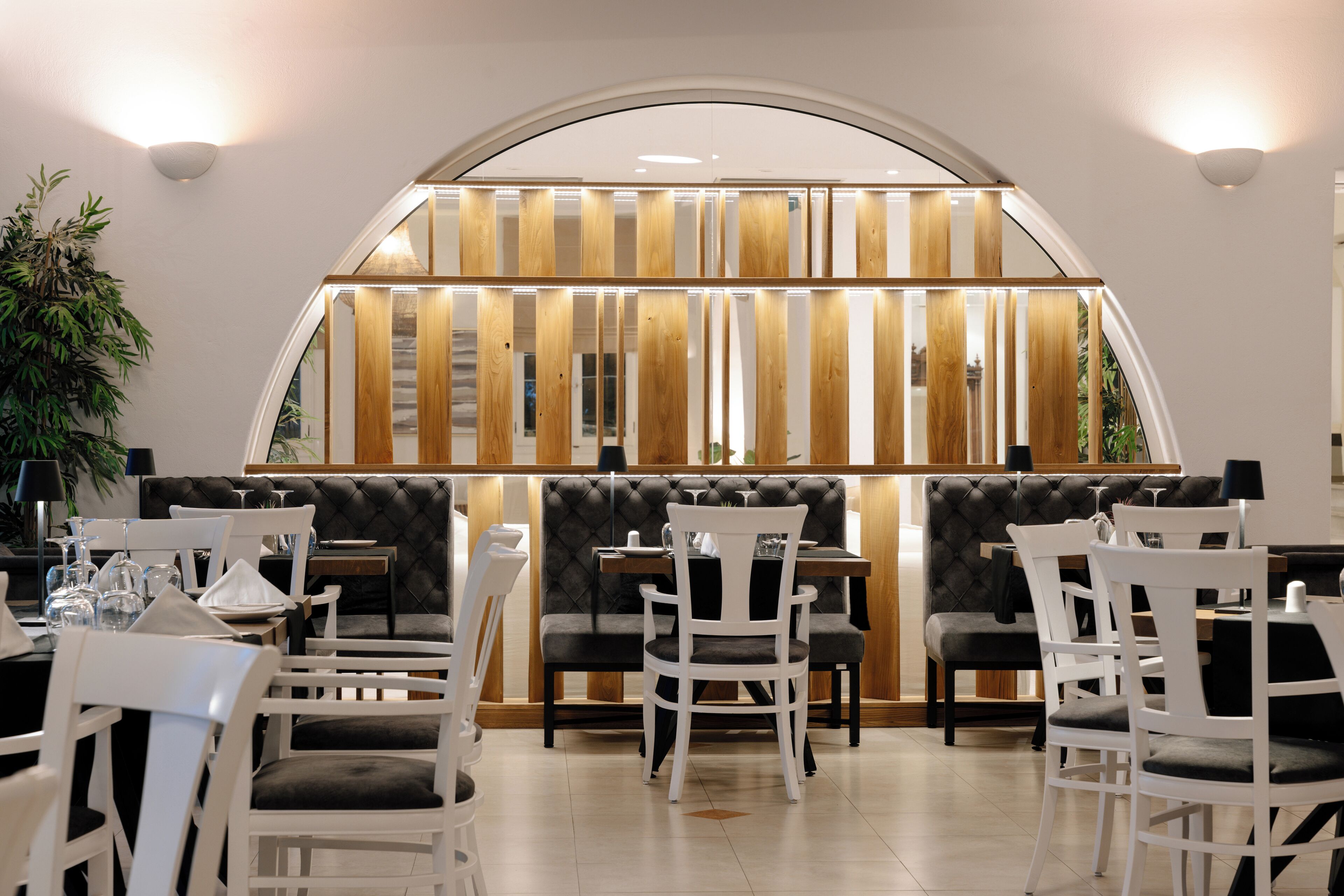 Un ristorante dall'arredamento moderno, con soffitto curvo, sedute imbottite e vista attraverso un'ampia finestra.