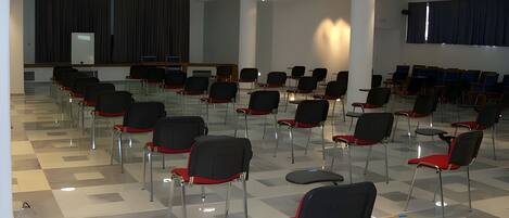 A conference room with rows of chairs, a stage, and a large screen.
