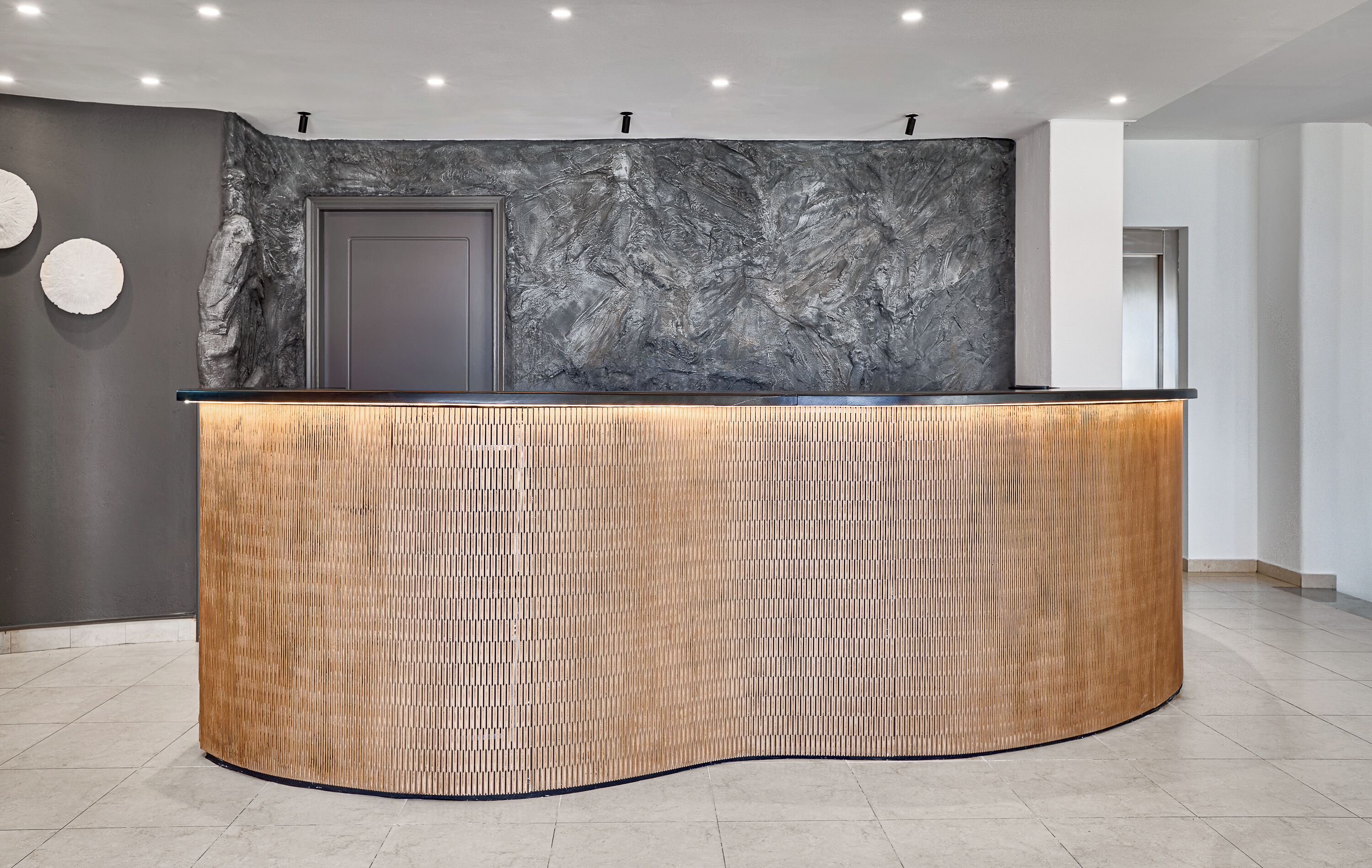 Un mostrador de recepción con textura de madera, una pared de mármol y una puerta.