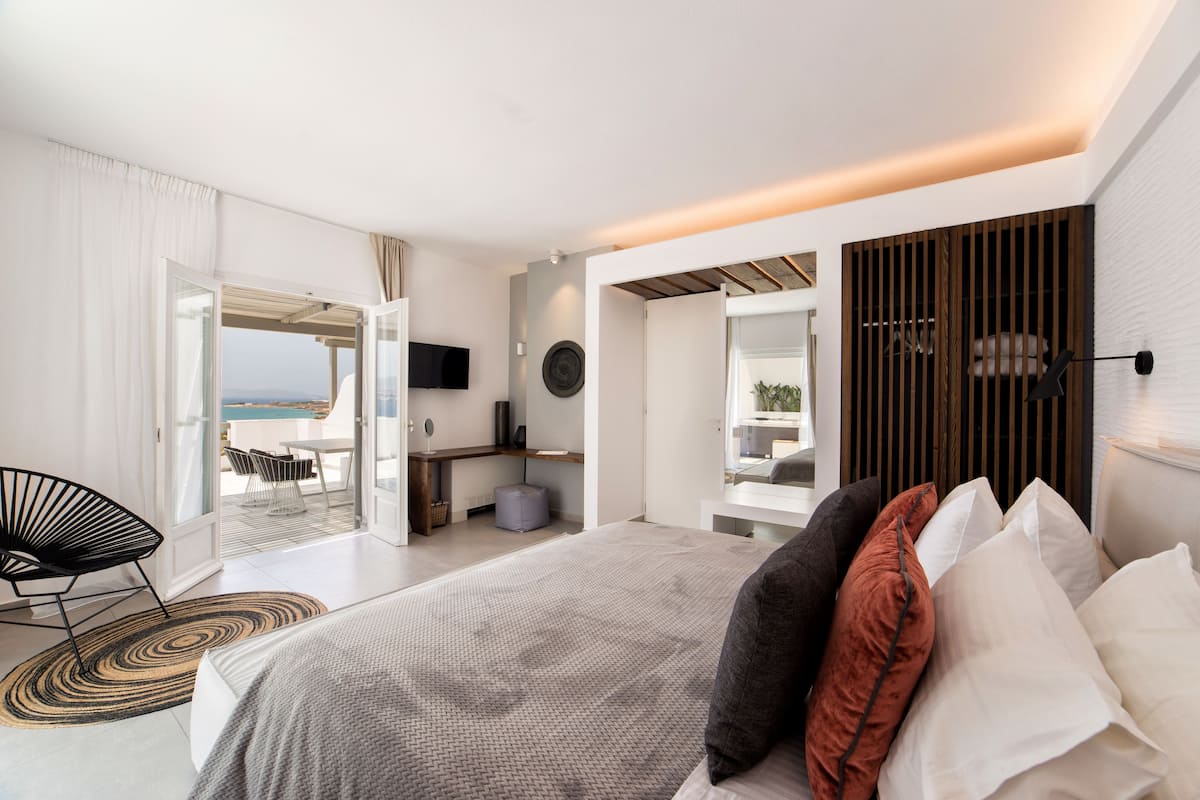 A modern hotel room with a large bed, a desk, and a view of the sea.
