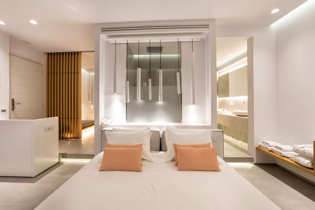 A modern hotel room with a large bed, a desk, and a bathroom visible through a glass partition.