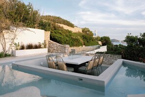 Una piscina con mesa y sillas, rodeada de muros de piedra y follaje.