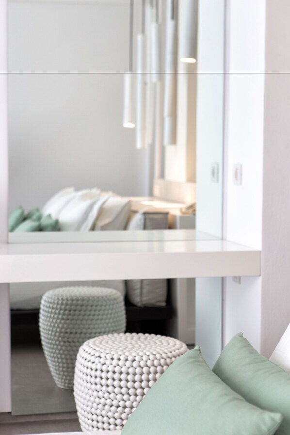 Un intérieur moderne avec une coiffeuse blanche, un miroir et deux petits bancs ronds.