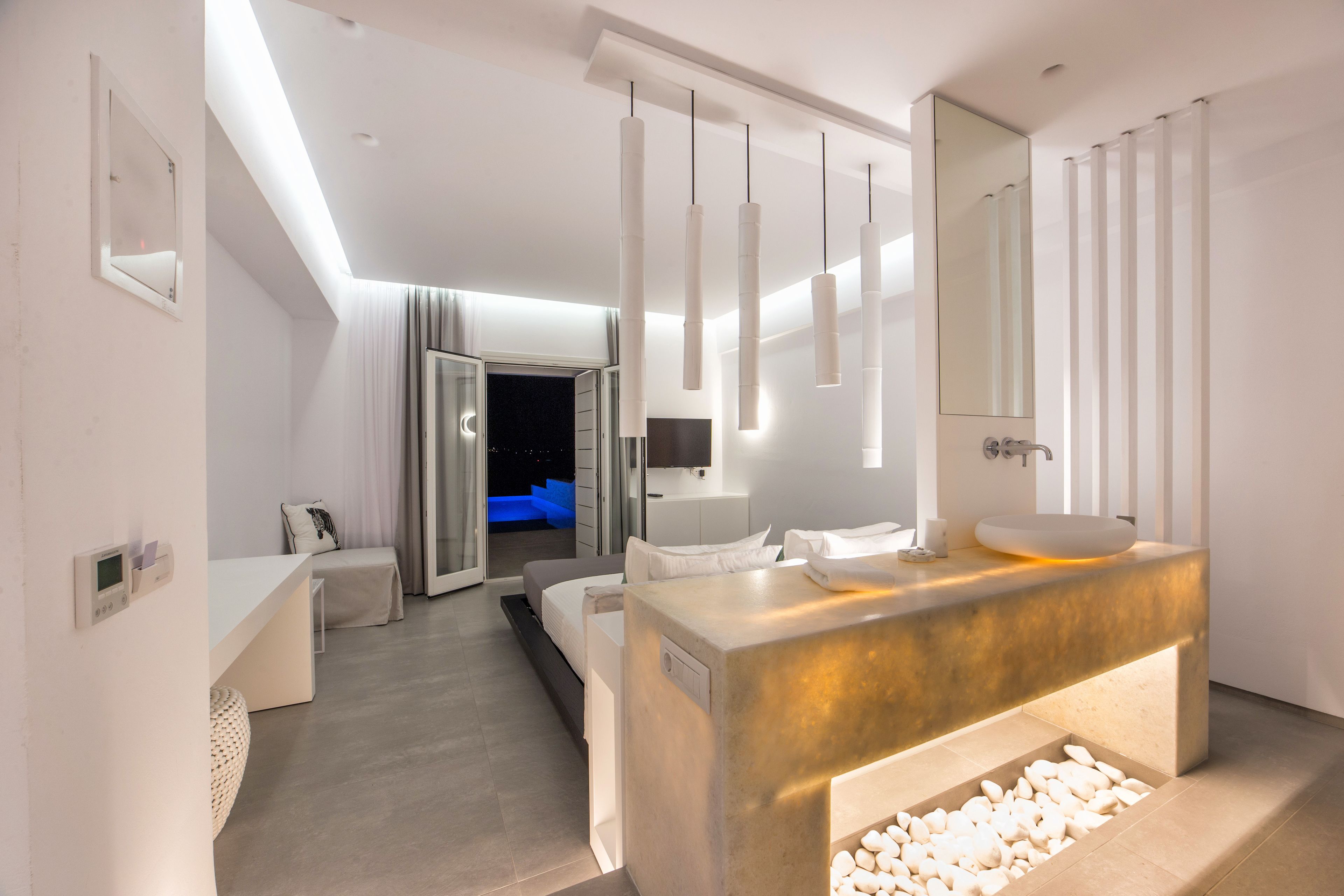 A modern hotel room with a large bed, a bathroom with a large mirror and a sink, and a view of the city at night.