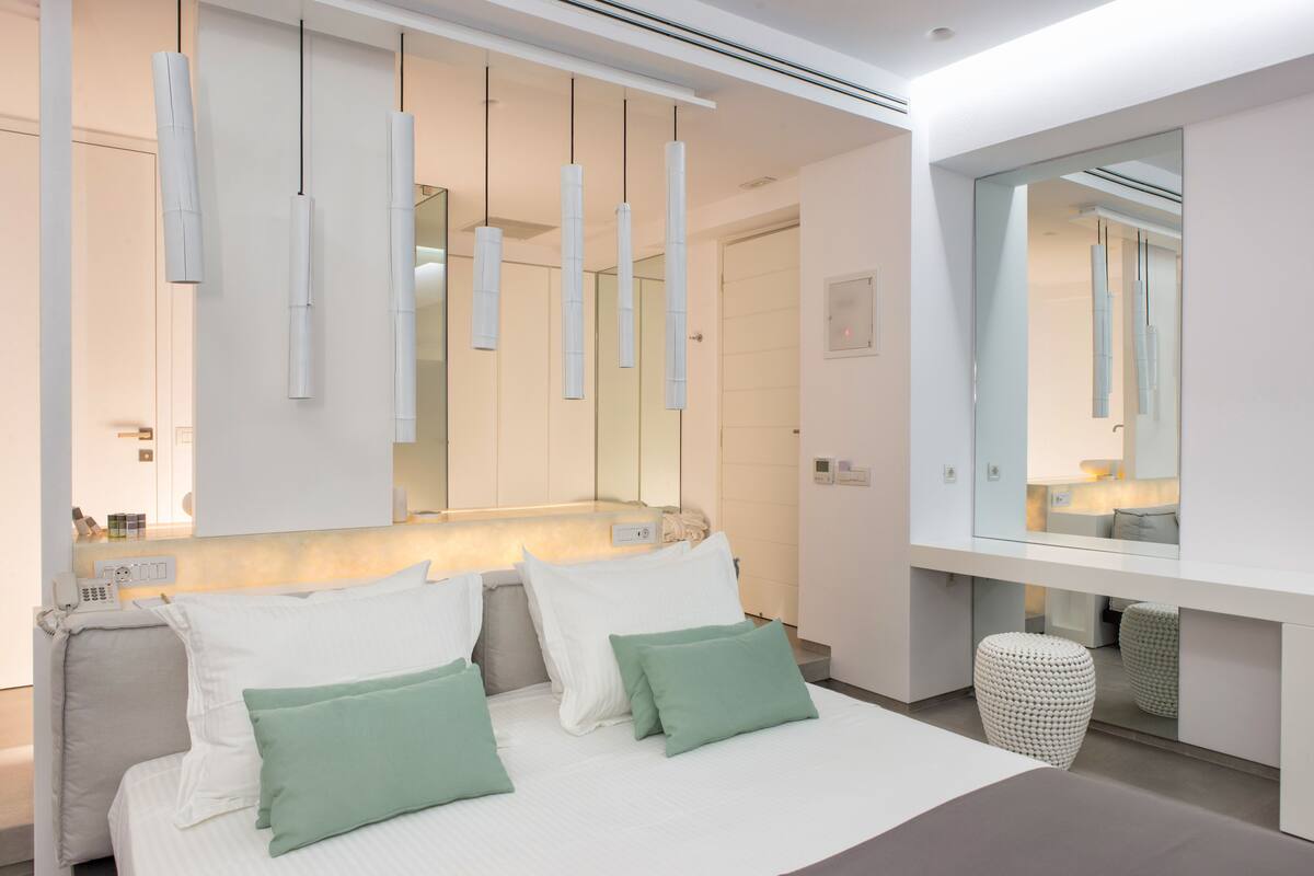 A modern bedroom with a large bed, bedside tables, a mirror, and pendant lights.