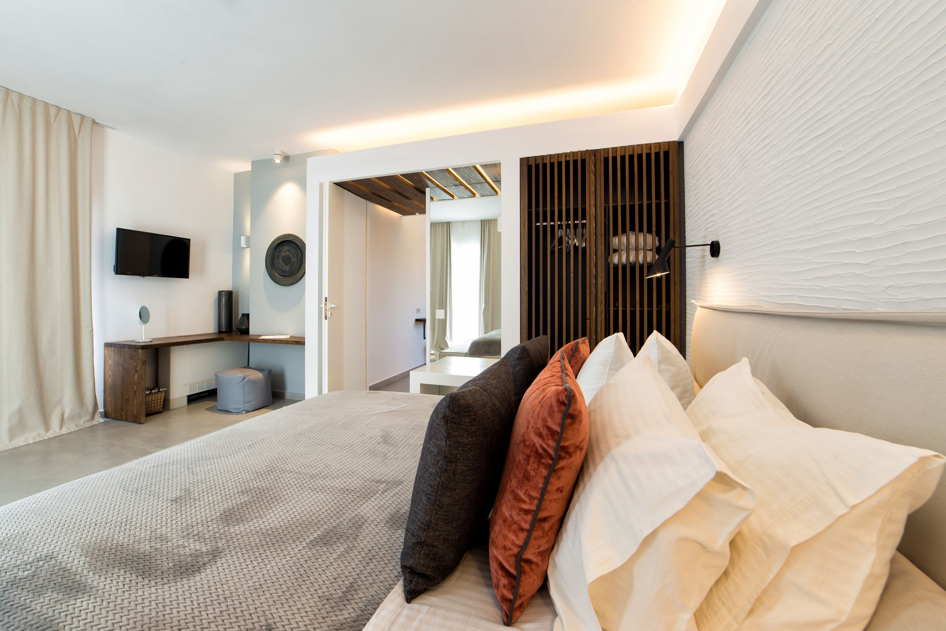 A modern bedroom with a large bed, a TV mounted on the wall, and a wooden slat partition.