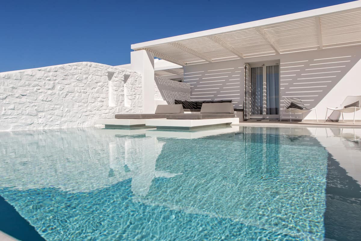A modern pool area with clear water, white stone walls, and contemporary outdoor seating.