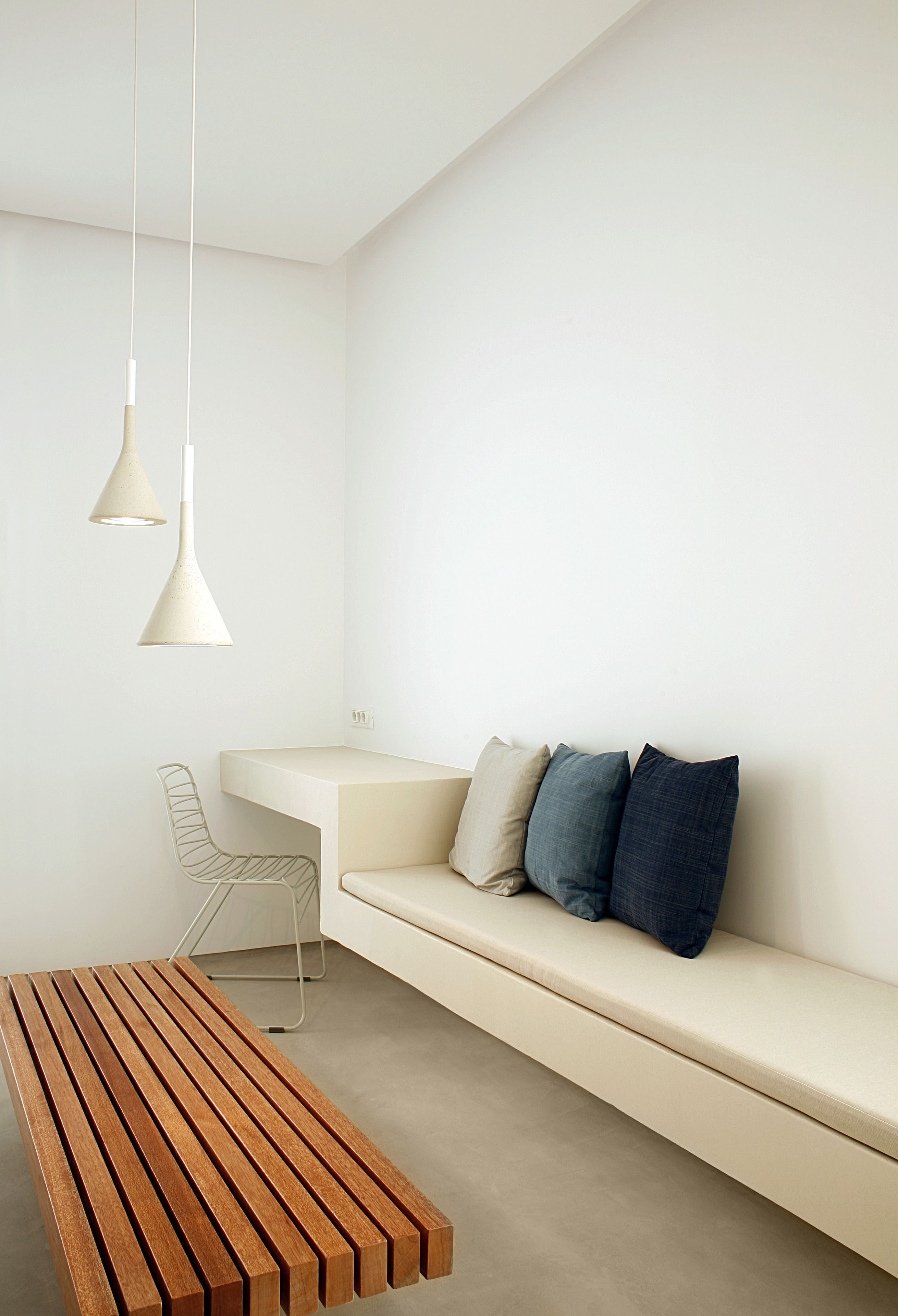 A minimalist room with a wooden bench, a white sofa with blue cushions, and two pendant lights.