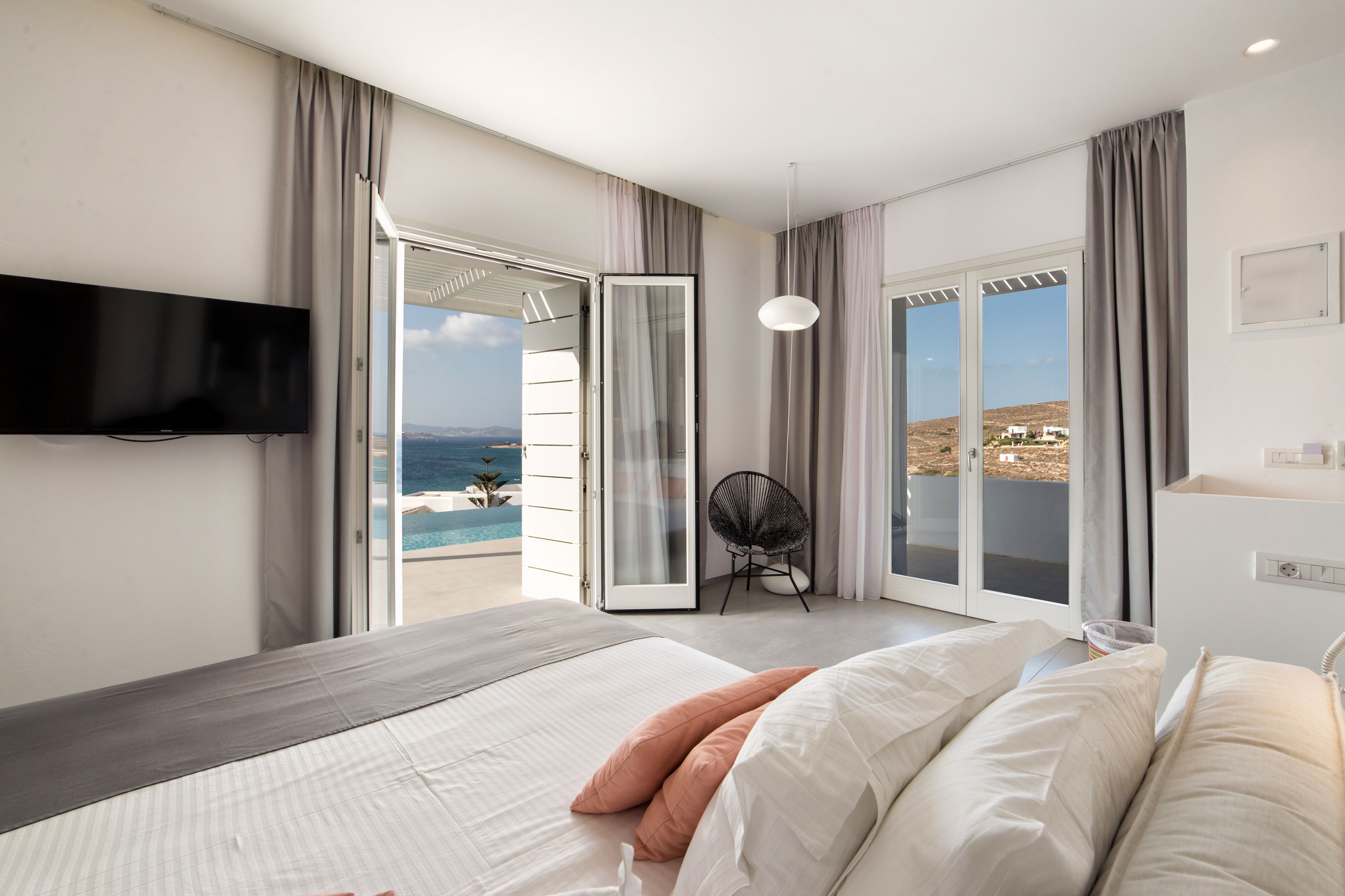Un dormitorio moderno con una cama grande, televisión, una silla y vista al océano.