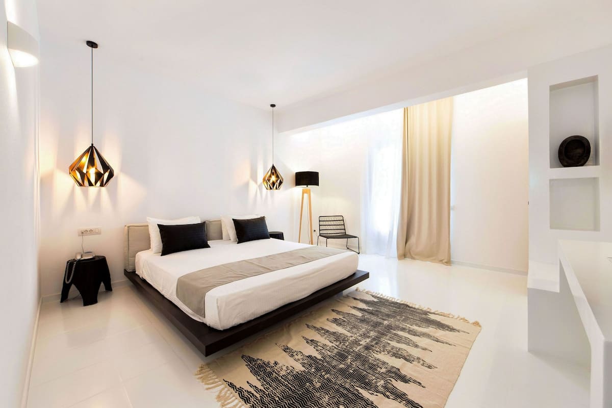 A modern bedroom with a large bed, a hanging light fixture, a standing lamp, and a minimalist decor.