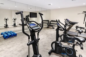 Un gimnasio con bicicletas estáticas, una cinta de correr y un televisor montado en la pared.