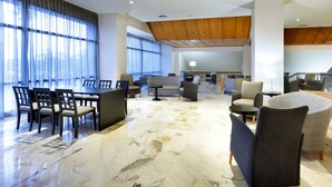 A spacious lobby with a marble floor, a seating area with chairs and sofas, large windows with curtains, and a wooden ceiling. - Hotel Exe Isla Cartuja (Seville)