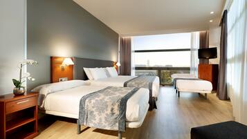 Habitación de hotel con dos camas, televisión, escritorio y balcón con vista a la ciudad.