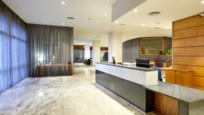 A modern reception area with a marble floor, a reception desk, and a wooden panel wall. - Hotel Exe Isla Cartuja (Seville)